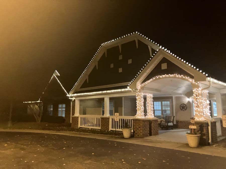 House exterior at night, decorated with white Christmas lights. Porch with wrapped columns and a walkway.