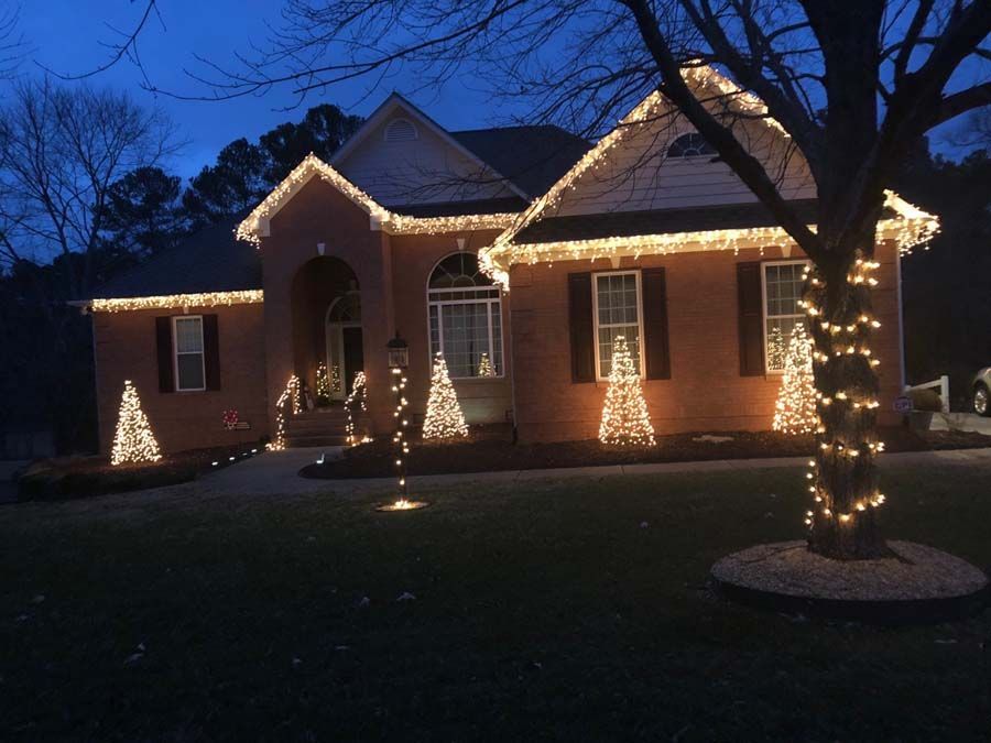 House decorated with Christmas lights, including roofline and trees, at dusk.