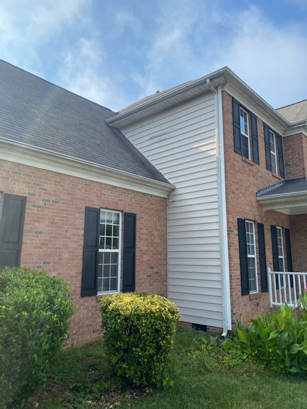 Brick and siding house with black shutters and green bushes