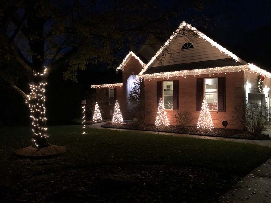 House decorated with Christmas lights at night. Tree and bushes wrapped in white lights.