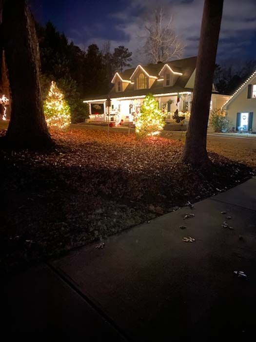 House decorated with Christmas lights at night, illuminated trees in yard.
