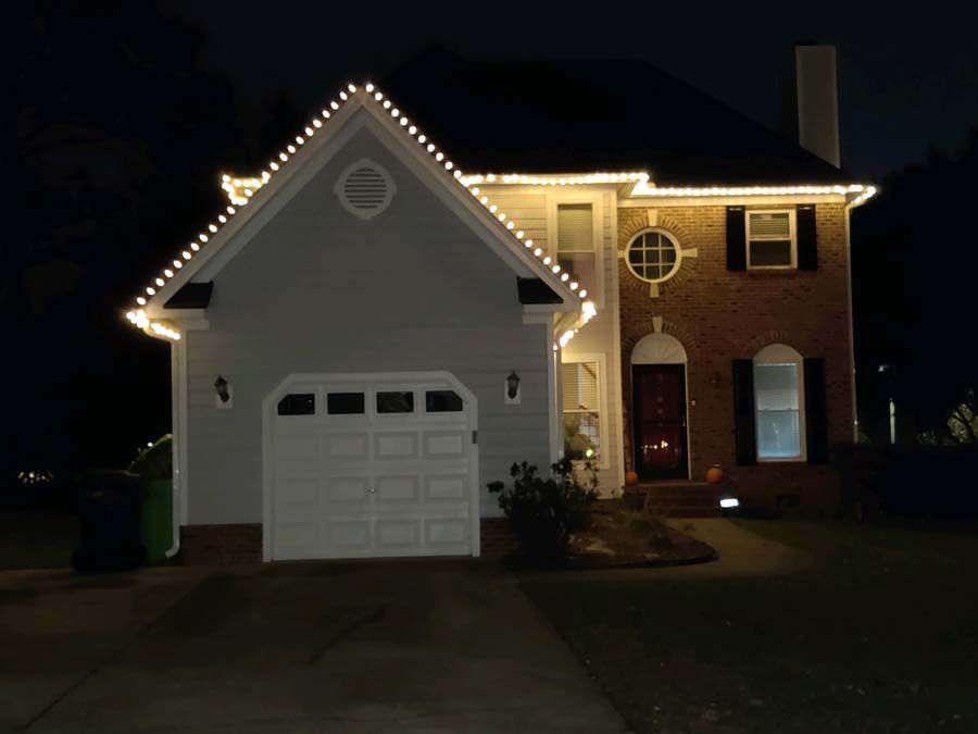House at night with white Christmas lights along the roof, with a garage and red door.