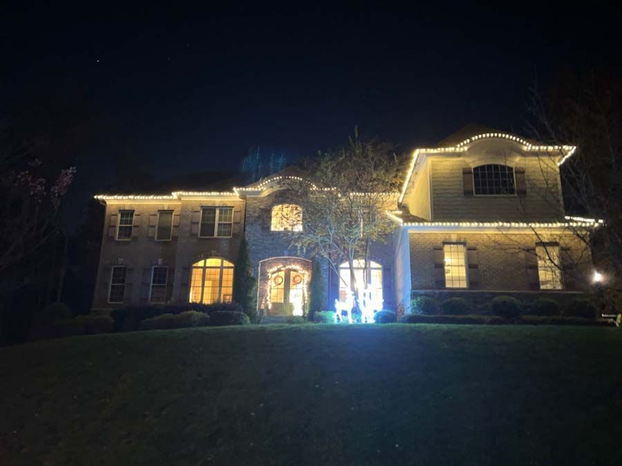 A two-story house at night, lit with yellow Christmas lights along the roof and around windows.