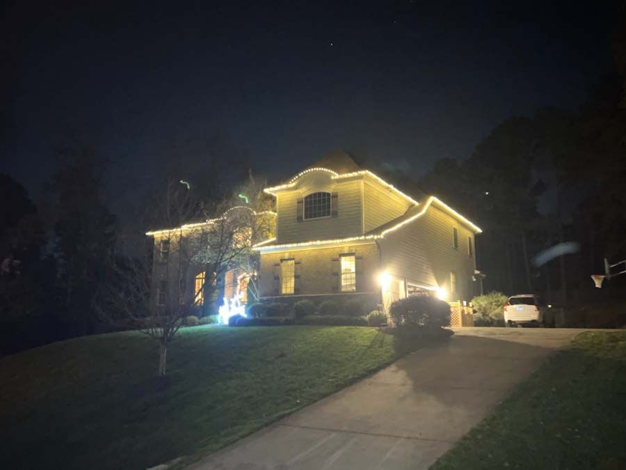 Two-story house lit with golden string lights at night, with a car parked in front.