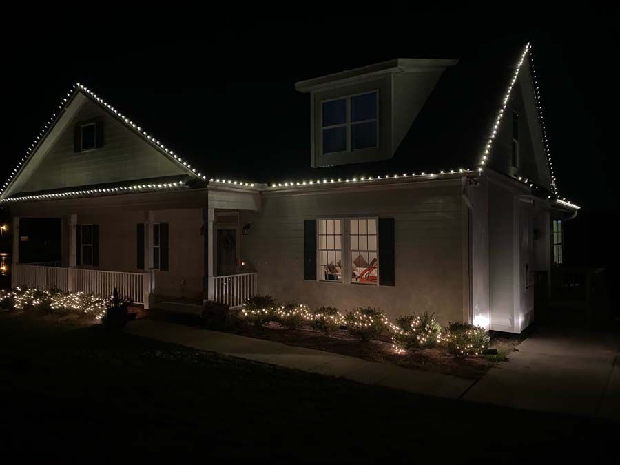 A house at night with white Christmas lights outlining the roof and bushes.
