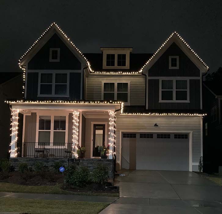 A two-story house lit with white lights along the roof and porch at night.