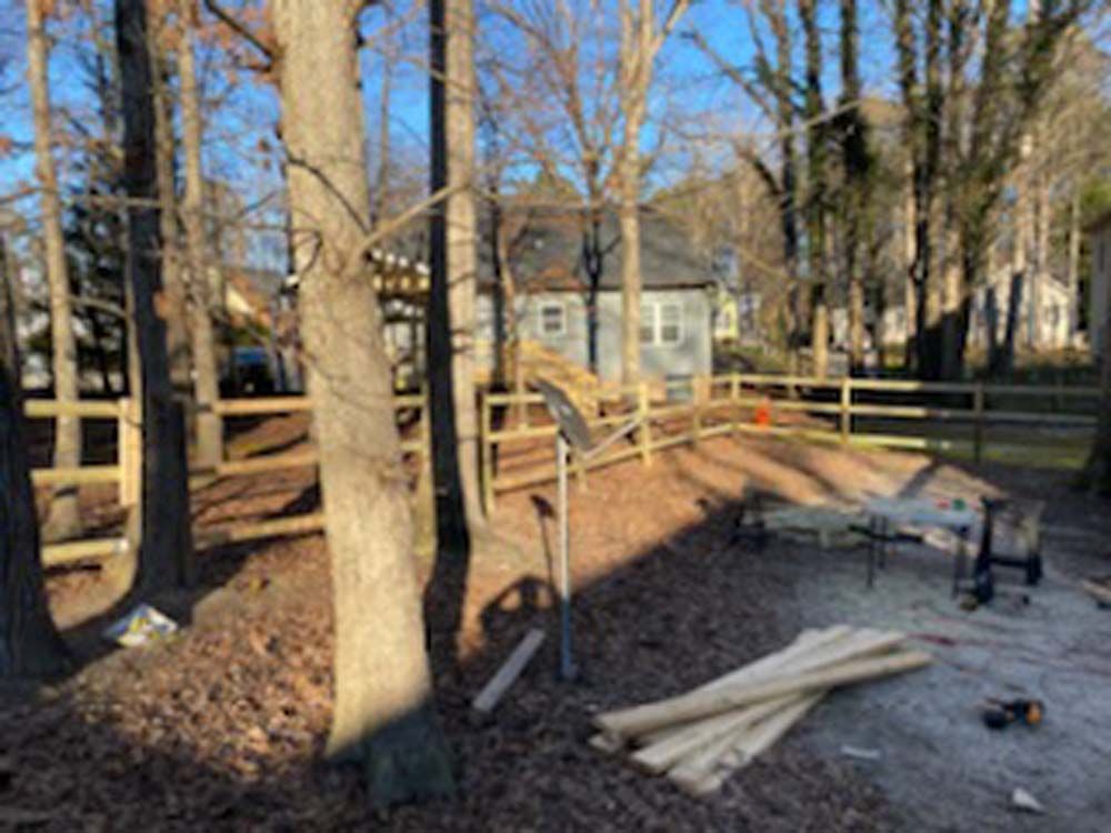 A wooden fence is under construction in a yard with a house in the background on a sunny day.