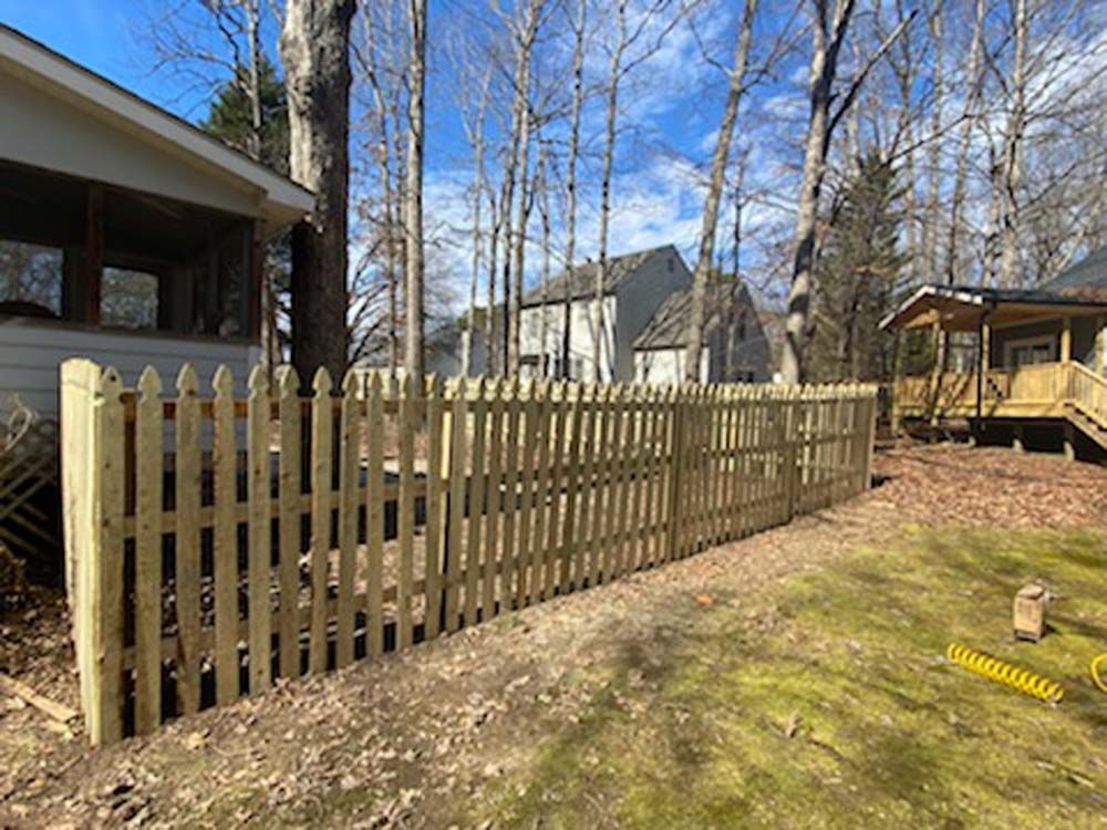 Wooden picket fence in a backyard with trees, grass, and houses in the background.
