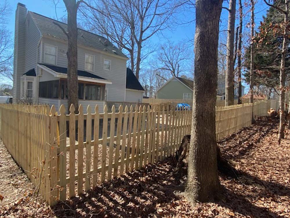 Wooden picket fence surrounding a two-story house on a sunny day.