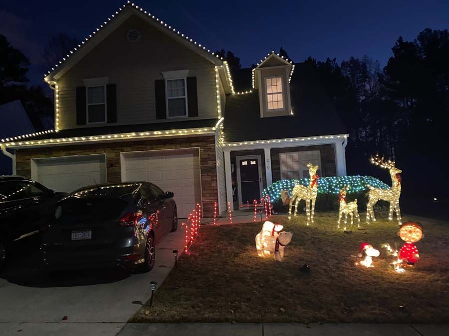 House decorated with Christmas lights and illuminated reindeer and other figures on the lawn at night.