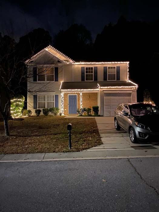 Two-story house at night with Christmas lights, blue door, and a car in the driveway.