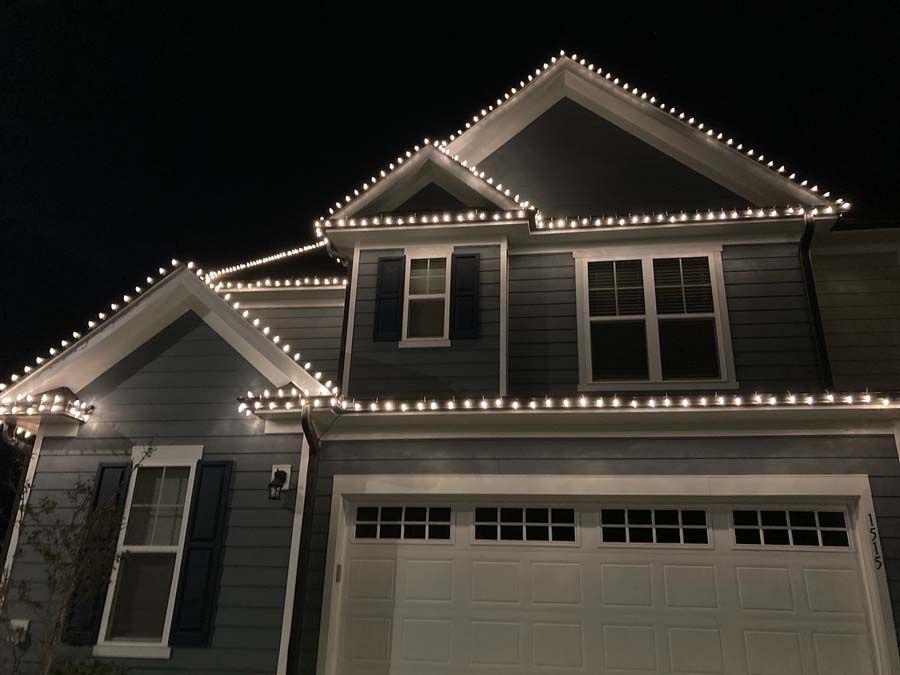 House with white Christmas lights outlining the roof and trim against a dark sky.