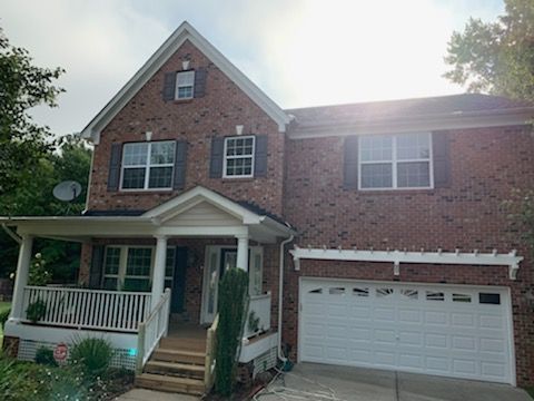 Two-story brick house with white trim, porch, and attached garage. Sunlight shines on the roof.