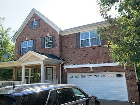 Brick house with white trim, gray shutters, two-car garage, and a vehicle parked in the driveway.