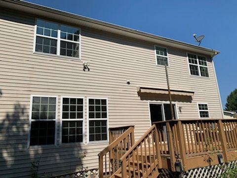 Back of a two-story beige house with a wooden deck, windows, and a satellite dish against a blue sky.