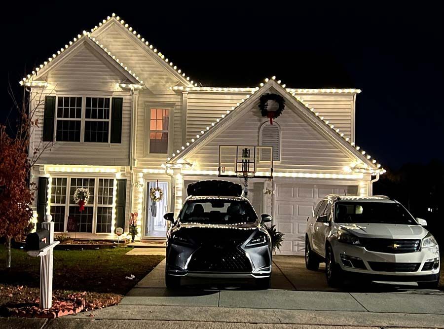 House and two cars decorated with Christmas lights at night.
