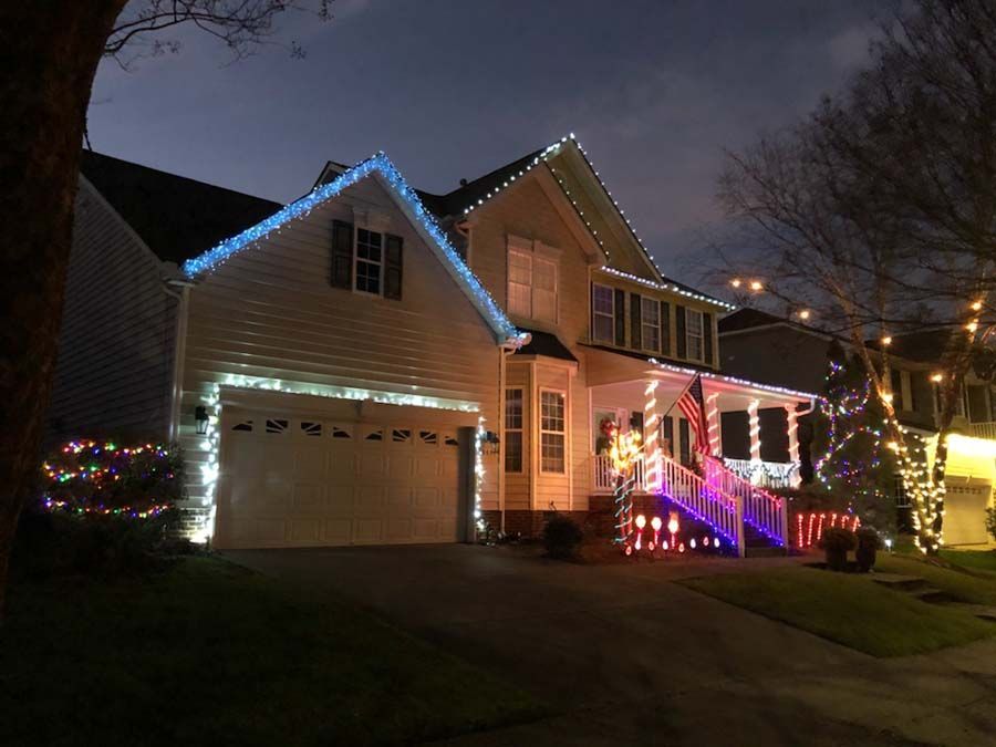 House decorated with blue, white, and red Christmas lights. Evening scene with lit porch and garage.