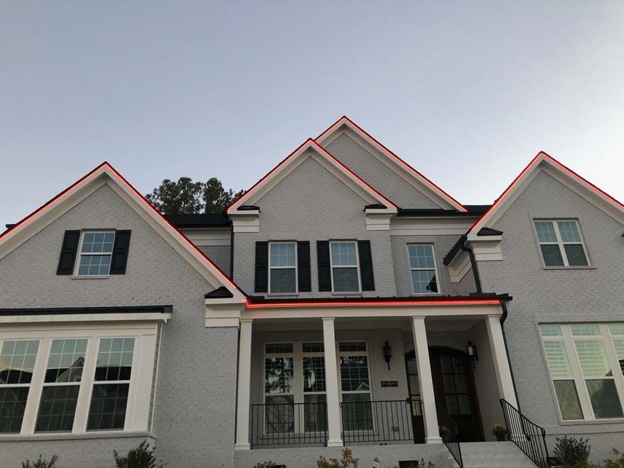 Gray brick house with red roof outline, black shutters, and porch.