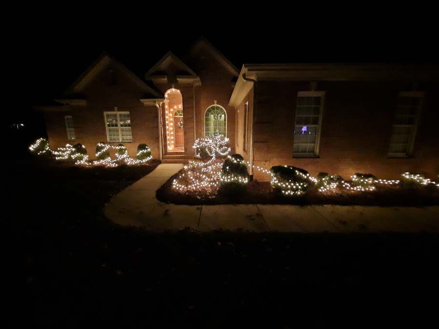 A brick house at night with Christmas lights decorating the bushes and doorway.
