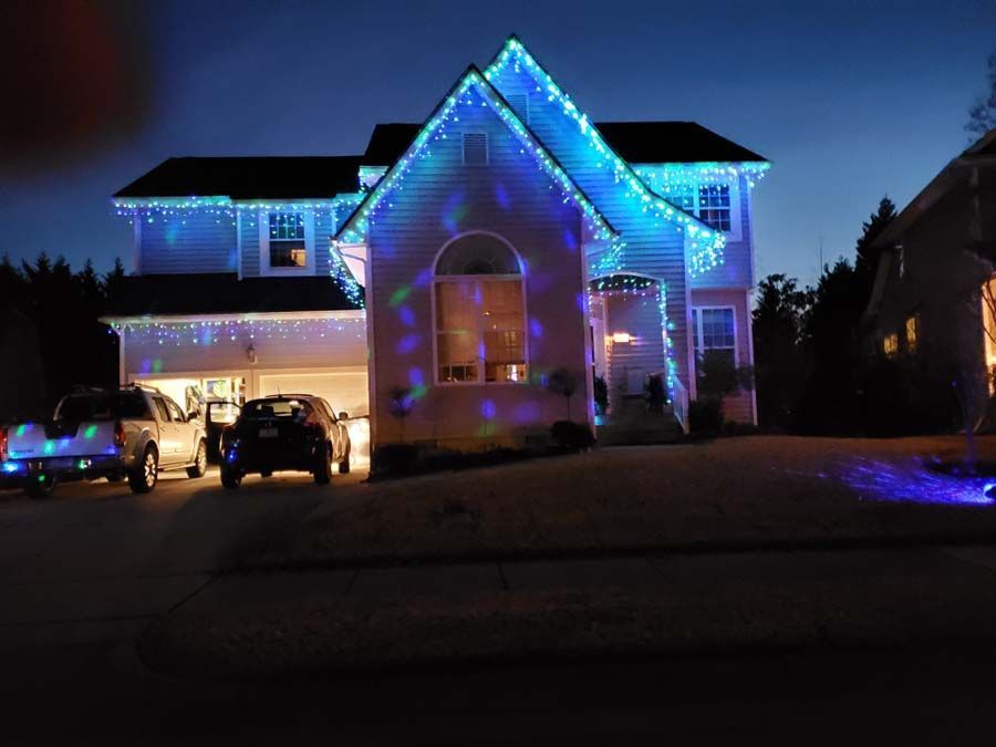 House with blue Christmas lights at night, illuminated cars in driveway.