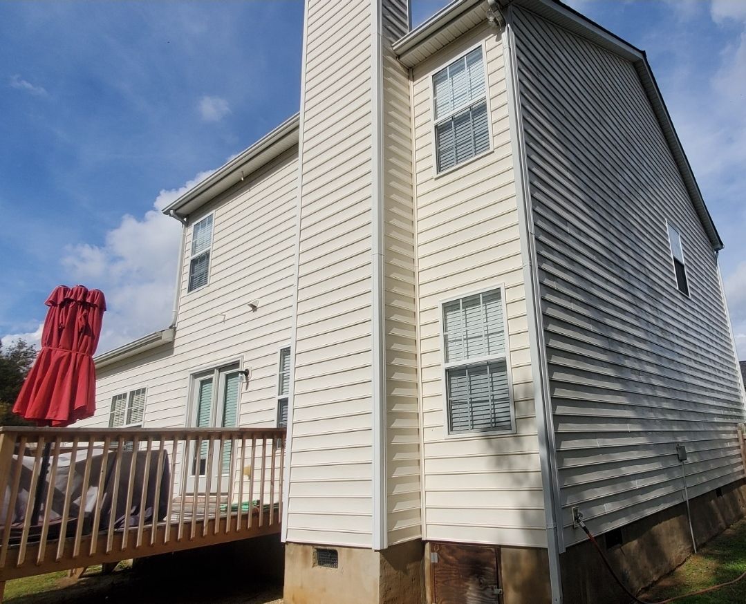 Two-story house with white siding, a wooden deck, and red umbrella against a blue sky