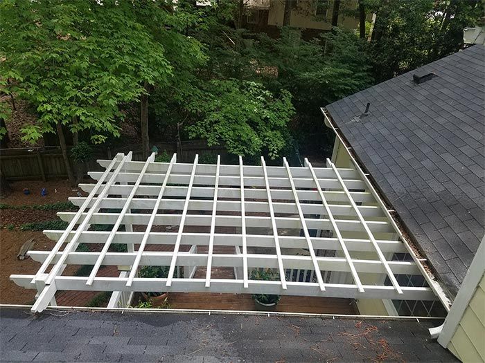 White pergola attached to a house, viewed from above, with trees in the background.