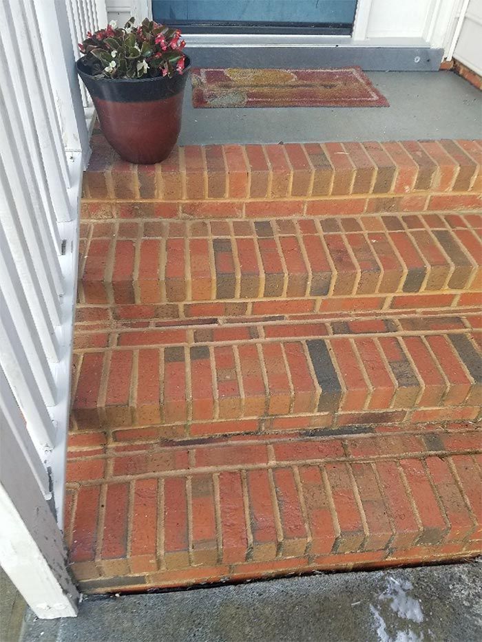Brick steps leading to a porch with a potted plant and a welcome mat.