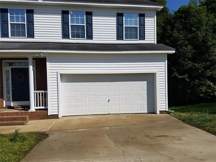 Two-story house with white siding, blue shutters, and a white garage door. Driveway in front.