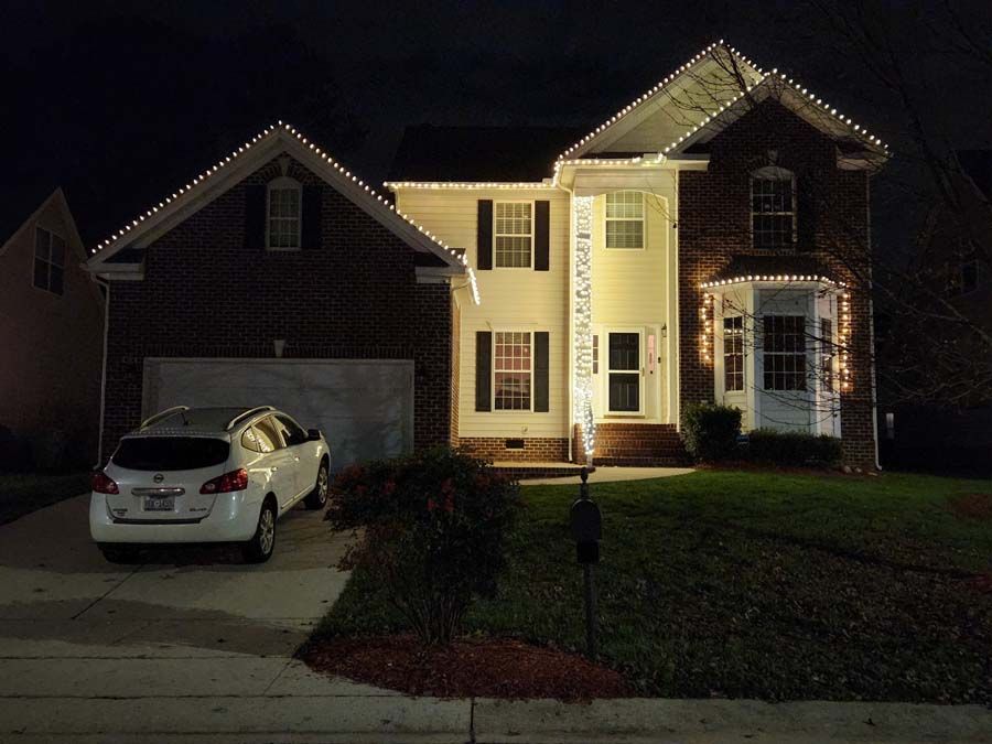 Two-story house at night with Christmas lights. White SUV in the driveway. Dark bricks, beige siding.