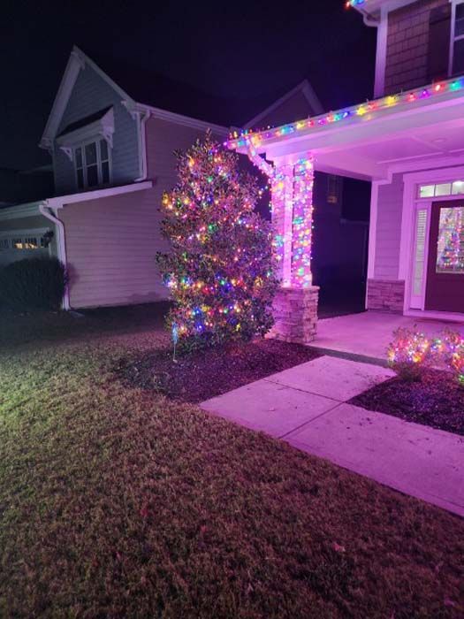 A house decorated with colorful Christmas lights, with a tree and porch columns illuminated at night.