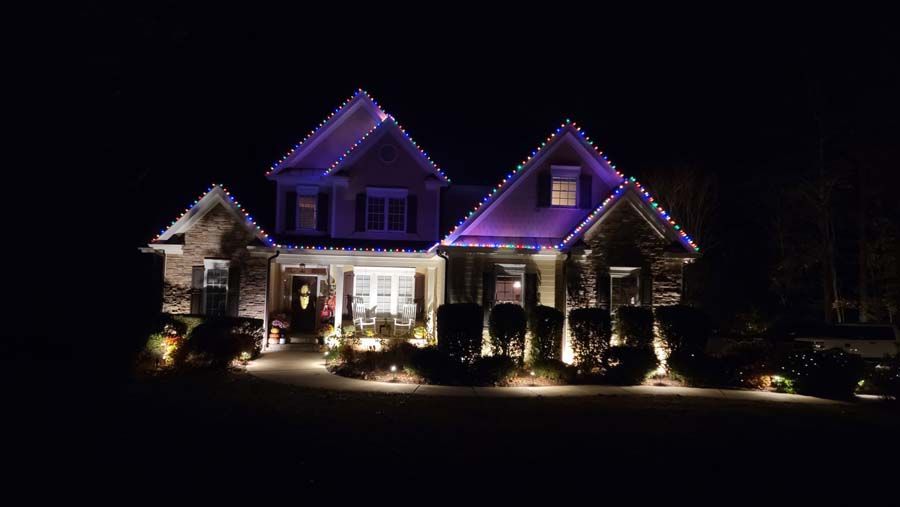 House lit with purple lights, bushes and walkway lit with warm lights at night.