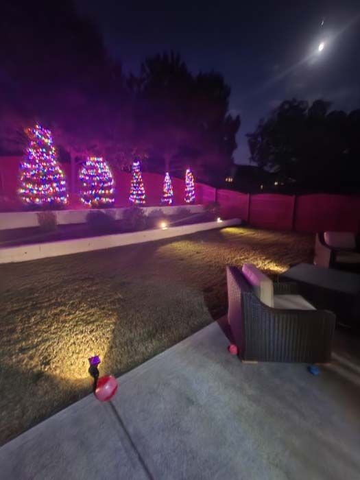Nighttime backyard with trees lit in pink and purple lights, patio furniture, and a full moon.