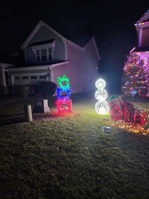 Christmas decorations in a yard at night: illuminated gifts, snowman, decorated tree.