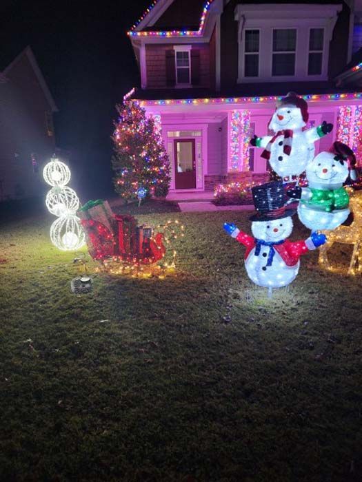 Christmas lights decorate a house, lawn features lit-up snowmen and a sleigh, all glowing at night.