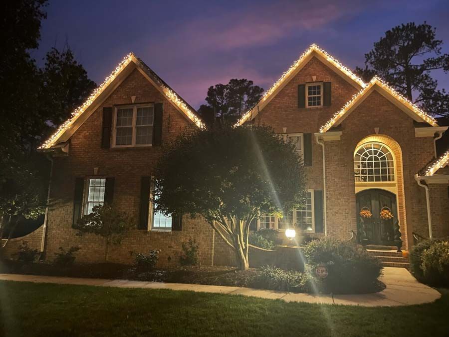 Brick house with Christmas lights along the roofline; dusk sky.