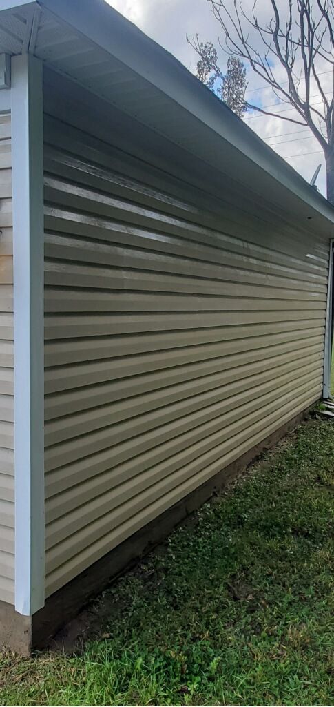 Tan vinyl siding on a building with a white trim and a dark brown base, cloudy sky.