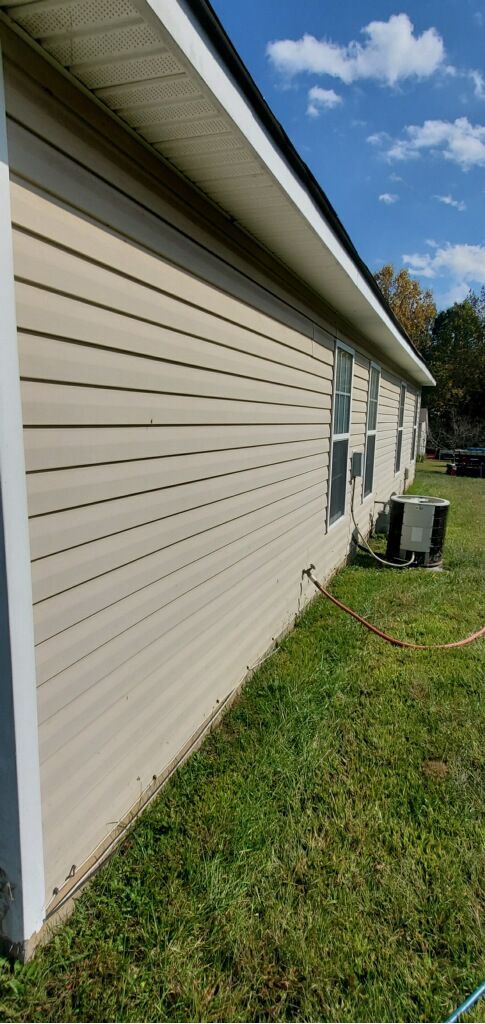 Side view of a beige house with white trim and a lawn. A/C unit on the side. Blue sky with clouds in background.