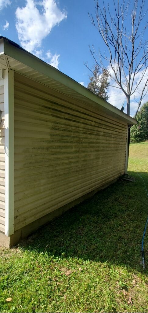 A building with green siding and roof against a blue sky with grass in front.