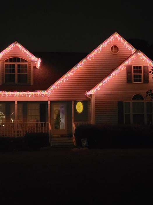 House at night illuminated with pink Christmas lights along roof.