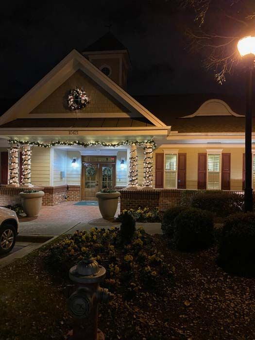 A building at night with Christmas lights, a wreath, and a lit lamp post.