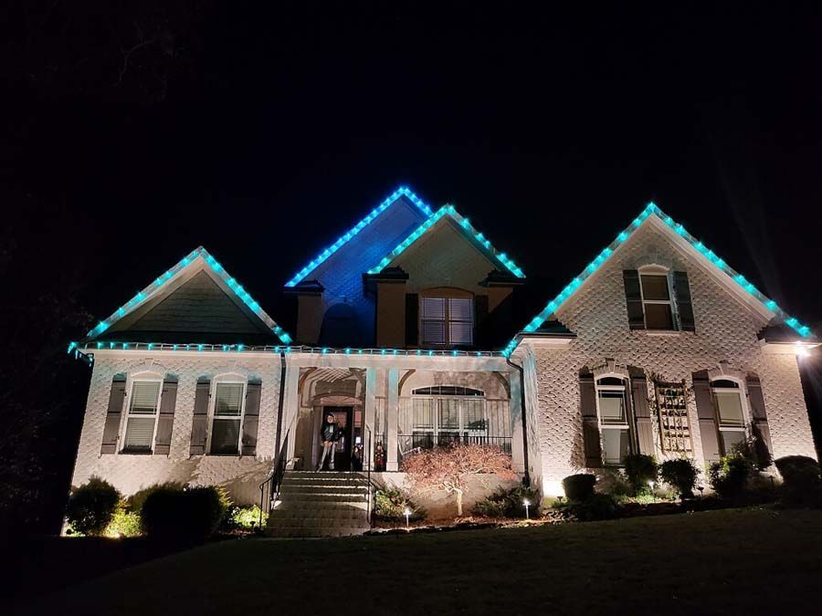 House at night with blue Christmas lights on the roof and spotlights illuminating the facade.