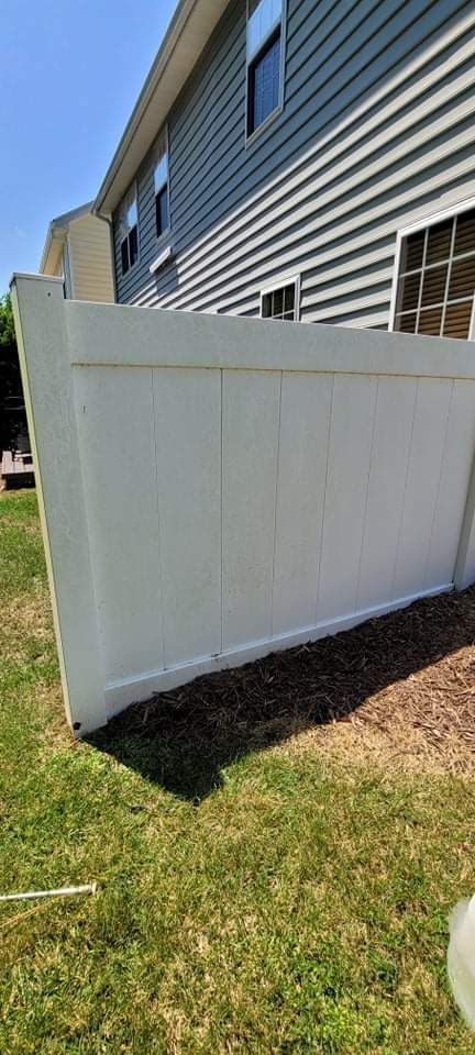 White fence next to a gray-sided building on a sunny day. Green grass below.