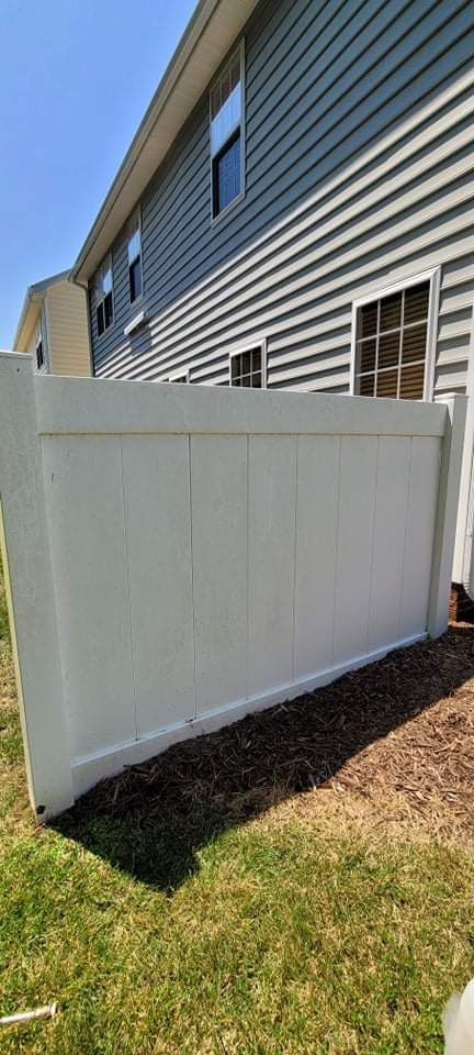 White fence next to a two-story building with gray siding and a grassy yard on a sunny day.