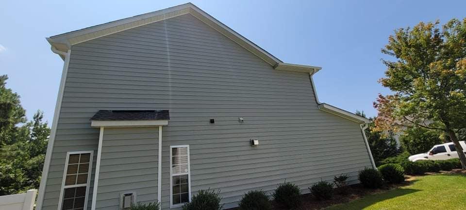 Side view of a two-story gray house with white trim, blue sky, and a truck parked in the yard.