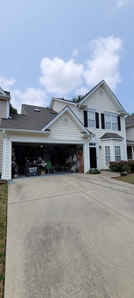 White two-story house with an open garage and long concrete driveway under a blue sky.
