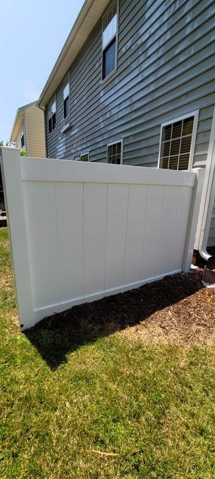 White fence next to a blue-sided building on a sunny day. Green grass is in the foreground.