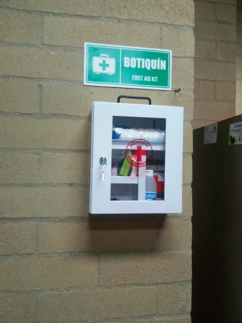 Botiquín blanco de primeros auxilios montado en la pared, debajo de un letrero verde con la palabra