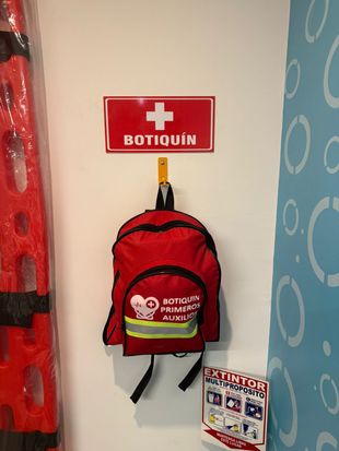 Una mochila roja de primeros auxilios cuelga debajo de un letrero blanco y rojo con la palabra