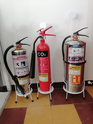 Tres extintores sobre soportes contra una pared blanca en una habitación interior.