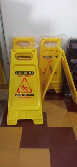 Señales amarillas de advertencia de suelo mojado en un pasillo, con suelo de baldosas rojas y pared blanca.